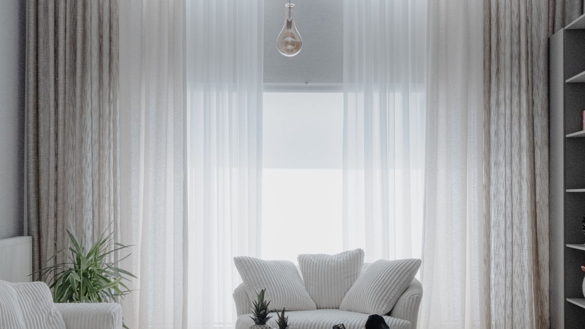 A bright staged living room with sheer curtains and simple furniture